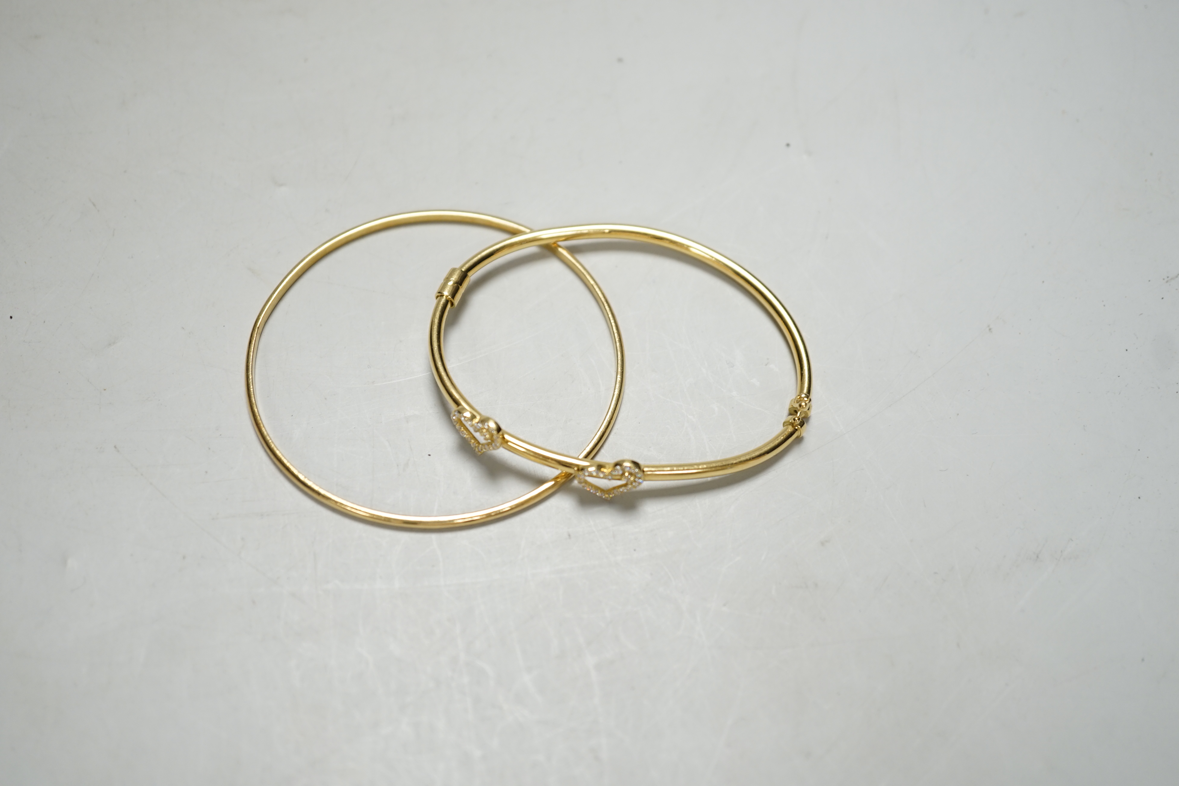 Two modern 750 yellow metal hinged bangles, one with diamond set twin hearts motif